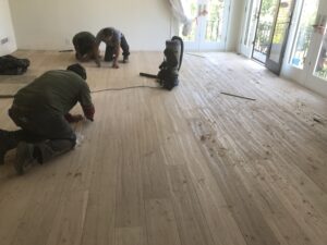 "Three flooring professionals using equipment to prepare newly installed Reclaimed hardwood floors for finishing."