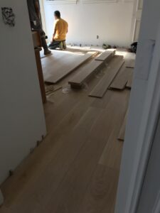 Installation of eco-friendly reclaimed hardwood floors made from salvaged oak wood, featuring distinct grain patterns and natural imperfections, in a modern living room setting.